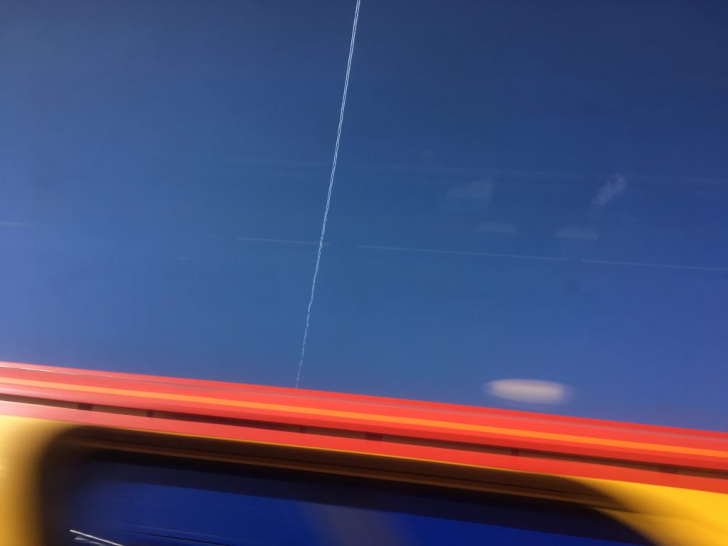 Central contrail cuts the blue sky over the roof of a passing train